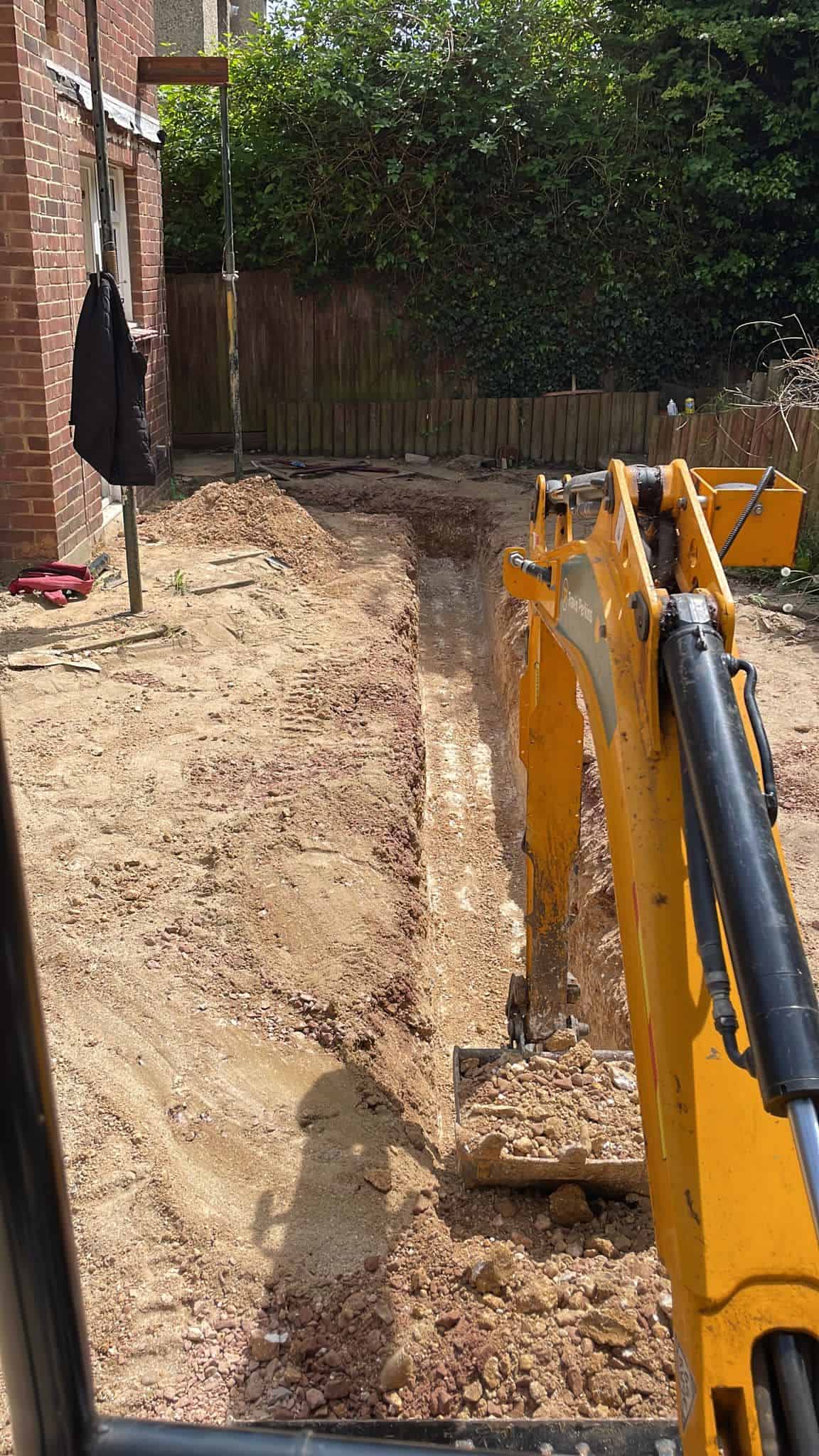 Yellow mini excavator digging trench in residential garden soil