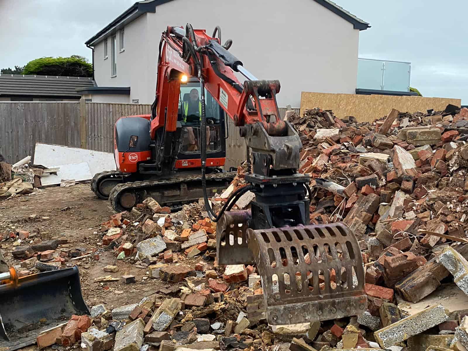 Red excavator demolishing brick rubble at construction site