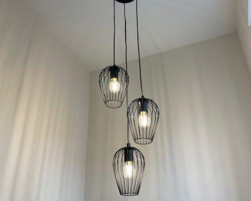 Modern black pendant light fixture with three wire cage shades in stairwell